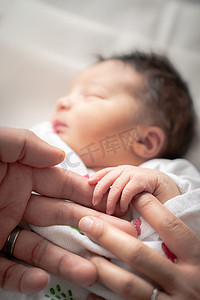 一个新生女婴在毯子襁褓中，用她的小手和手指包裹着父亲和母亲的手指，安然入睡。
