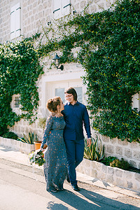 新娘和新郎沿着马路拥抱，靠近一栋有白门的老建筑，墙上缠绕着绿色的藤本植物