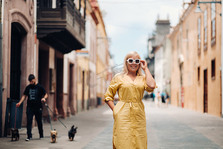古女子摄影照片_一位身穿黄色夏装的金发女子站在特内里费岛拉古纳老城的街道上。西班牙，加那利群岛