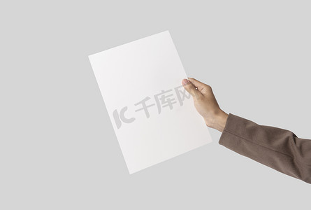 冲刺传单摄影照片_手在灰色背景上展示空白纸 A4 传单，用于样机模板徽标品牌。
