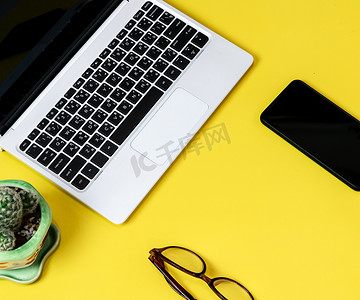 笔记本电脑放置在商业工作场所的黄色桌子背景上，配有一杯咖啡，空工作区