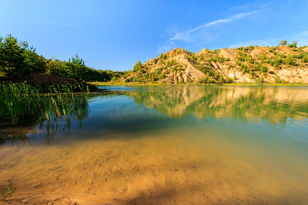 采石场或湖泊或池塘，有沙滩、绿水、树木和蓝天的山丘