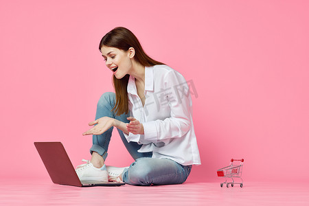 坐在地板上、带笔记本电脑购物娱乐粉红色背景的女人