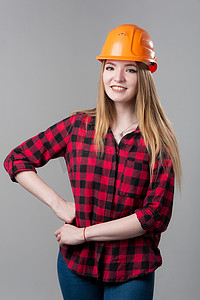 一位年轻漂亮的女人的肖像，金发，戴着橙色头盔，背景为中性灰色。