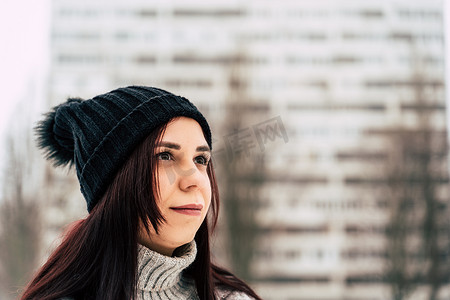 冬季穿着灰色针织毛衣和帽子站在街上的体贴的年轻女人。