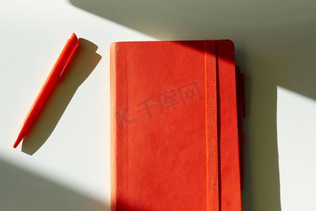 红色手册手册摄影照片_红色笔记本记事笔太阳光白色桌子