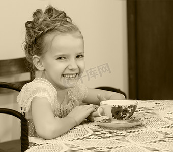 可爱的小杯子摄影照片_可爱的小女孩在旧桌旁喝茶。