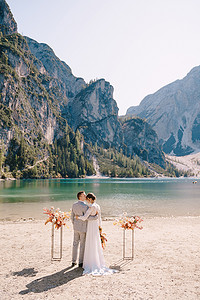 白云站摄影照片_新娘和新郎在意大利 Lago di Braies 的背景下，以秋天的花柱拱门为仪式站好。