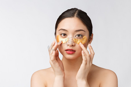 亚洲美女少女在眼睛下方用金色眼罩贴片护理皮肤