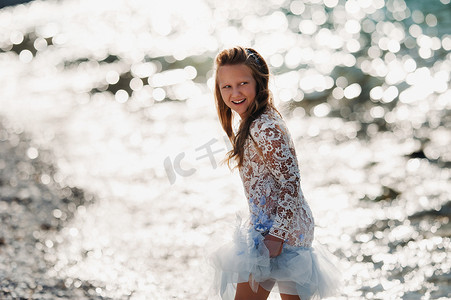 一个穿着漂亮白色连衣裙的小女孩沿着加尔达湖的堤岸行走。一个女孩在意大利的山和湖的背景下被拍照。托尔博莱