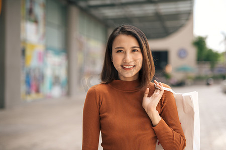 在户外商场提着购物袋的快乐亚洲年轻女性画像