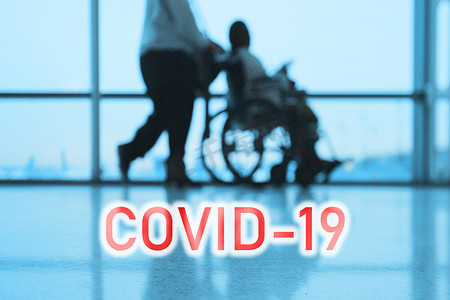 蓝色医院背景上的COVID-19广告牌红色文字，医生与坐在轮椅上的残疾病人一起行走
