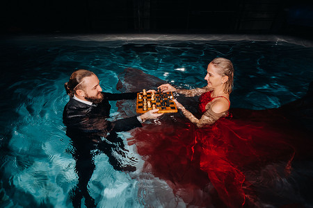 一个穿西装的男人和一个穿红裙子的女孩在游泳池的水面上下棋