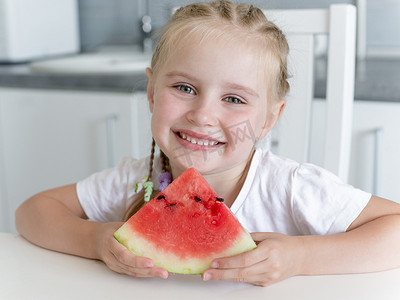 可爱西瓜摄影照片_可爱的小女孩在厨房里吃西瓜