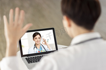 医生与他的同事进行视频通话的后视图。微笑的医生表现出 ok 的手势。