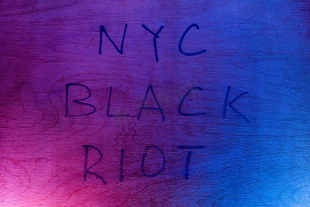 在红色和蓝色警灯下，平坦的胶合板表面上用黑色油漆标记手写了“纽约黑色骚乱”的字样。