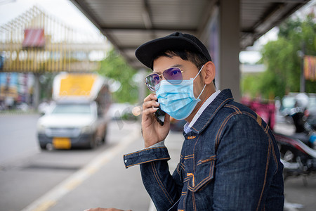 亚洲年轻人在城市使用智能手机并戴口罩，以保护空气污染、颗粒物和保护流感病毒、流感、冠状病毒