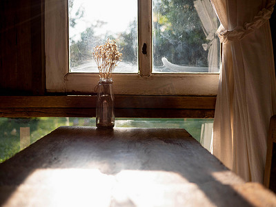 房间窗户附近的木桌上有干花瓶，晚上阳光充足。