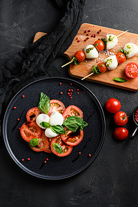 卡普雷塞沙拉番茄和马苏里拉切片，罗勒叶放在棍子串上，黑色陶瓷平台黑色纹理背景顶视图