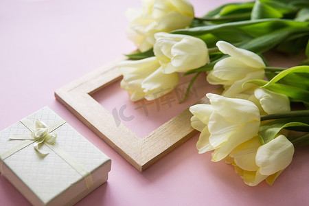 黄色郁金香花、相框和礼品盒排列在粉红色背景上。