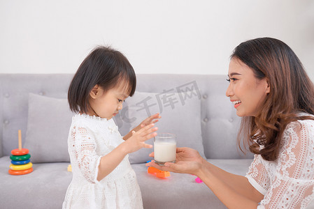 喝牛奶摄影照片_小女孩和她妈妈坐在家里的沙发上喝牛奶。