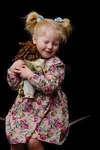 一个小女孩在黑色背景下玩洋娃娃。