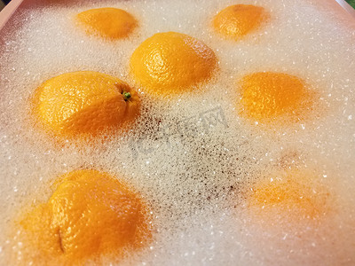 塑料桶摄影照片_粉红色塑料桶中肥皂水中的橙子