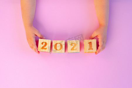一个孩子的手拿着粉红色背景的 2021 年木方块