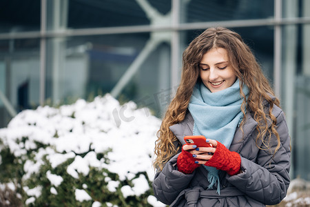 站在冬季城市街道上的智能手机上的卷发女性发短信。
