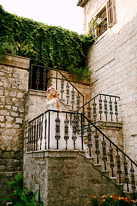 在科托尔老城的楼梯上，一位戴着白色和粉红色玫瑰花环的新娘站在楼梯上，楼梯上有锻造栏杆