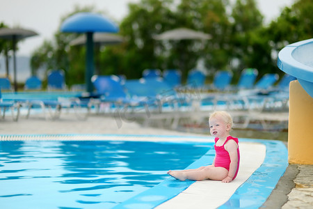 幼儿游泳摄影照片_坐在游泳池边的可爱幼儿女孩