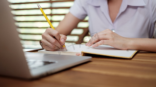 在笔记本电脑上工作时，年轻女孩用笔在记事本上写下启发灵感的想法列表
