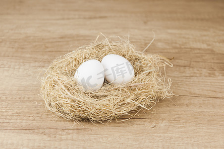 椭圆形不规则图形摄影照片_木桌上的巢里有白色的鸡蛋，有复制空间