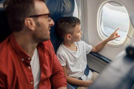 和父亲一起乘飞机旅行时，好奇的小男孩看着窗外