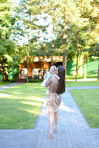 迷人背影摄影照片_在公园里抱着小婴儿的黑发女人的背影。