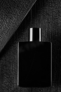 这是一张深色淡香水或香水的宣传照片。一棵烧焦的树背景上的黑色瓶子