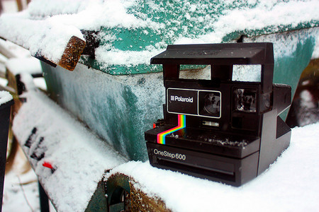 宝丽来相机矢量摄影照片_一张宝丽来 One Step 600 放在一个白雪覆盖的蓝绿色金属容器附近