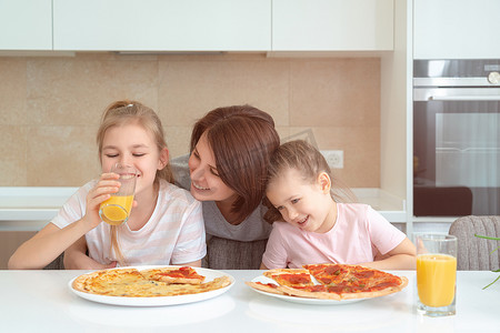母亲和两个女儿在厨房的桌子上吃自制披萨，幸福的家庭观念