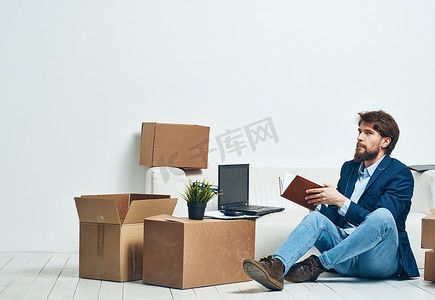 一个男人坐在一个盒子的地板上，里面有东西办公室正在搬家拆包官员