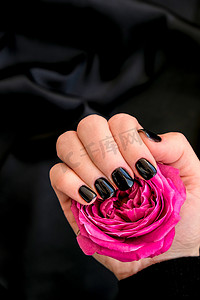黑色指甲修指甲将粉红色玫瑰花放在黑色丝绸织物上。