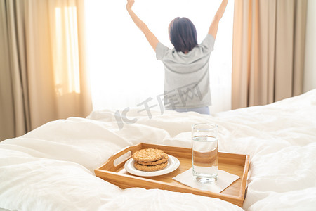 床上放着节食早餐的托盘，背景是女人伸懒腰