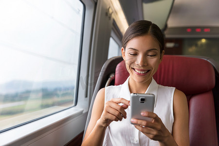 快乐的亚洲女商人在乘火车上班时使用手机应用程序发送短信或玩视频游戏。
