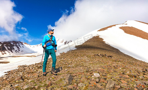 肩上扛着相机的登山摄影师凝视着雪山之巅。
