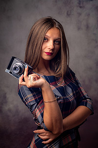 一个手里拿着相机的漂亮女孩的肖像，灰色背景中的半身工作室肖像