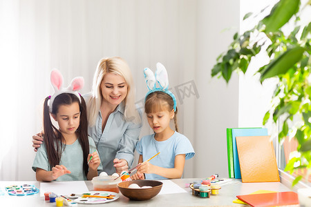 元宵节彩蛋摄影照片_年轻的母亲和她的两个小女儿在家画彩蛋