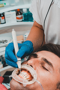 医学实践摄影照片_牙科实践，牙医在超声波的帮助下去除牙齿上的结石和硬斑块，患者口腔内有牵引器和唾液喷射器。