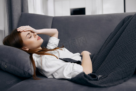 女性盖着毯子睡觉摄影照片_盖着毯子的女人躺在沙发上，手放在头上感觉不舒服