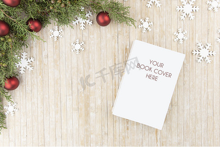 圣诞平躺顶视图，供一本书展示：带空白封面、松树枝、白色木制雪花和浅色木桌上的红色小饰品的书