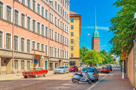 赫尔辛基 — 2019 年 6 月，芬兰：一条有车流的街道、Mikael Agricola 教堂和色彩缤纷的住宅楼