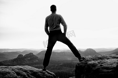 双手插在口袋里的黑衣运动员站在岩石帝国公园的山顶上，看着薄雾